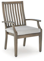 Wooden arm chair with slatted back, curved armrests, and light beige seat cushion.
