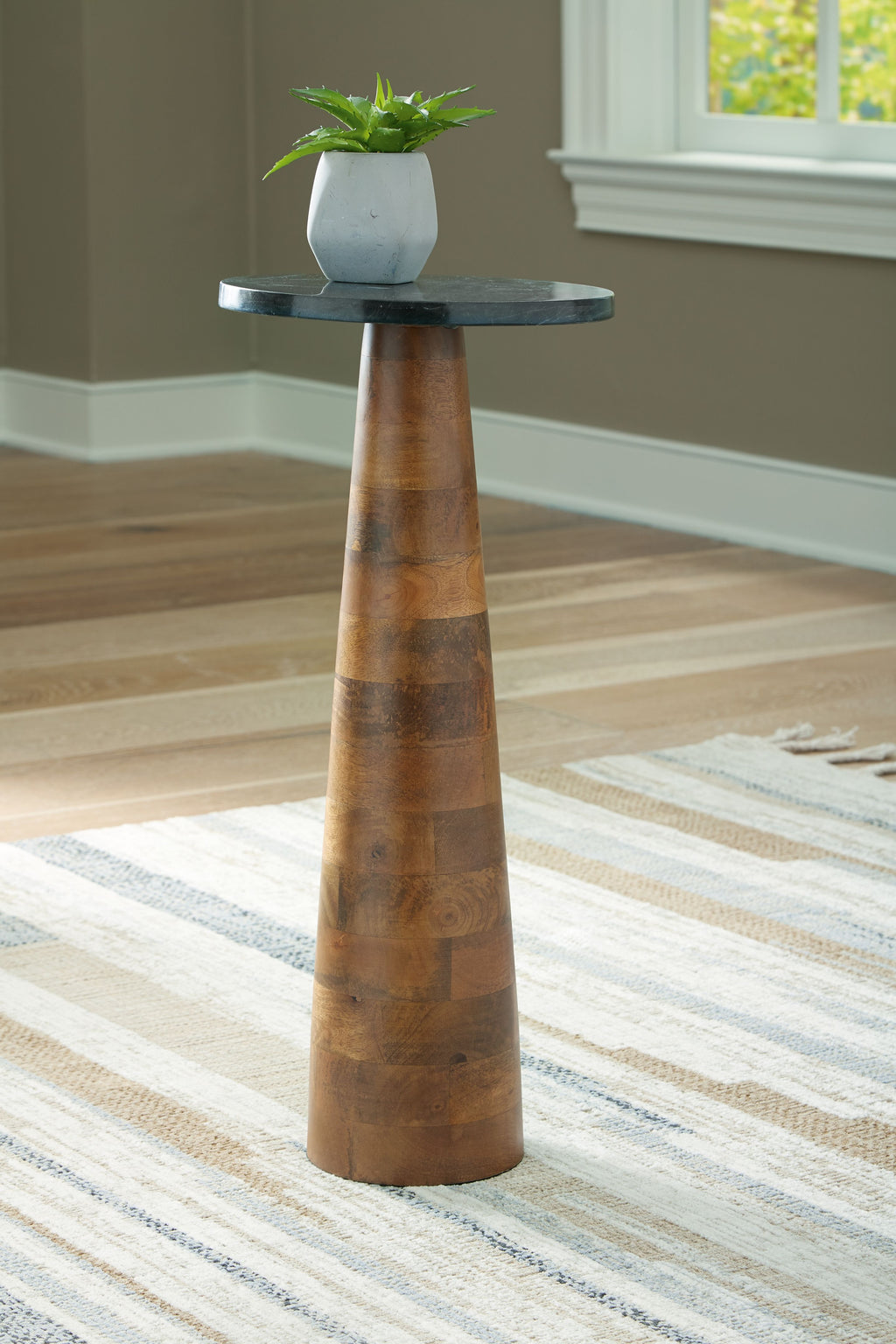 Round black stone-look accent table with narrow pedestal base in brown wood