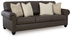 Dark brown sofa with four beige patterned throw pillows, rolled arms and tufted detailing
