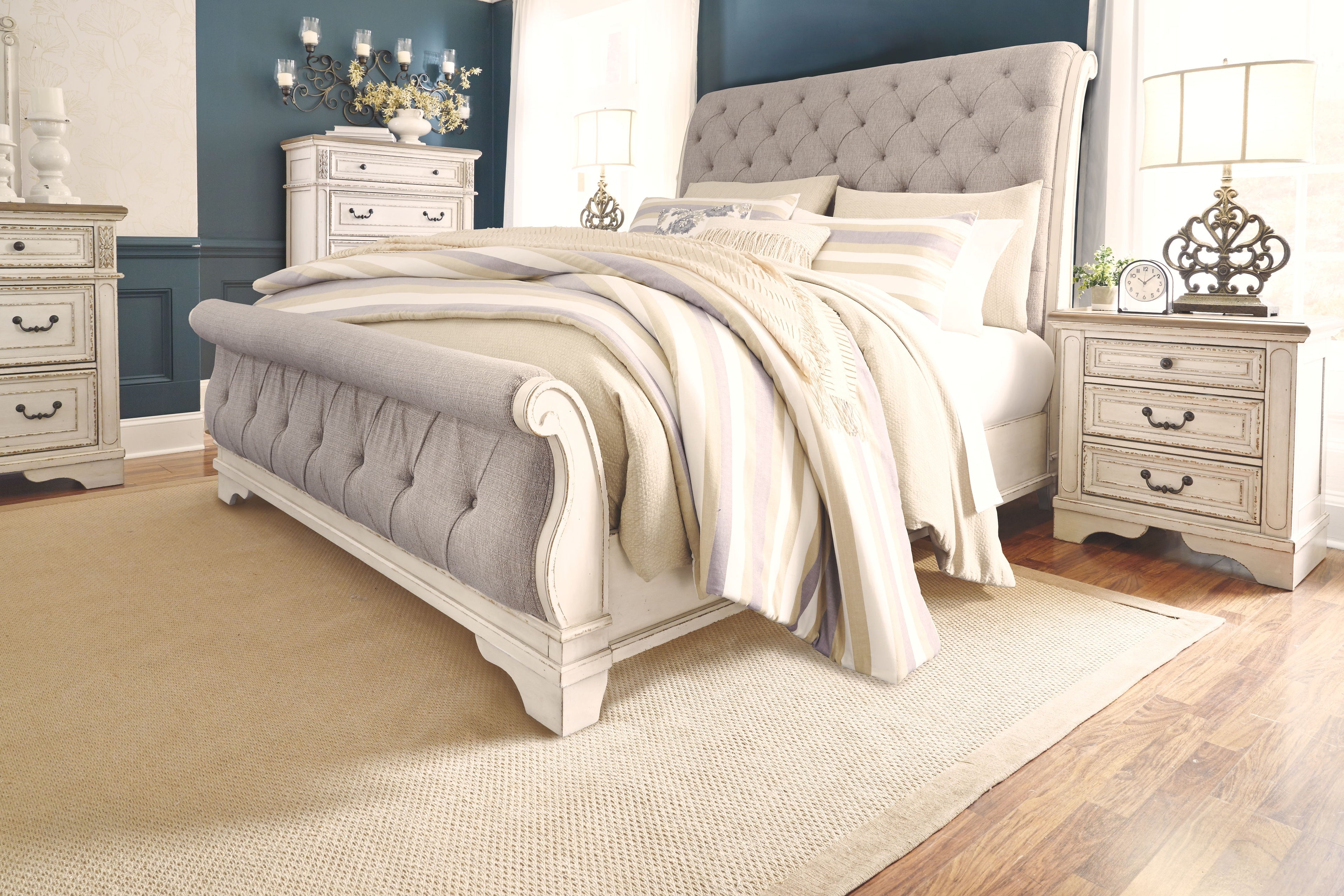 White sleigh bed with tufted headboard and side rails, featuring layered striped bedding