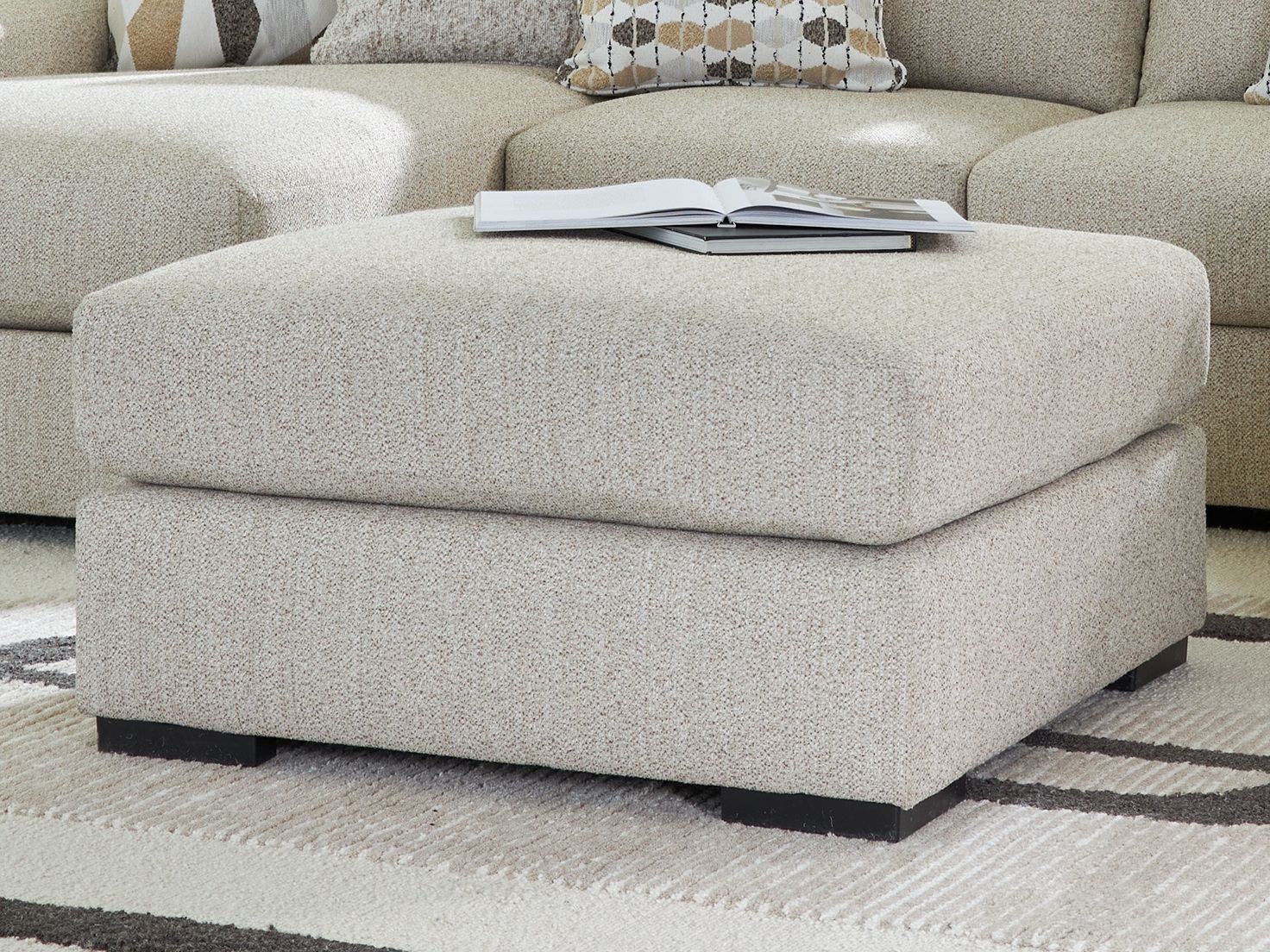 Oversized accent ottoman with thick cushion and dark legs, light pebble woven upholstery.