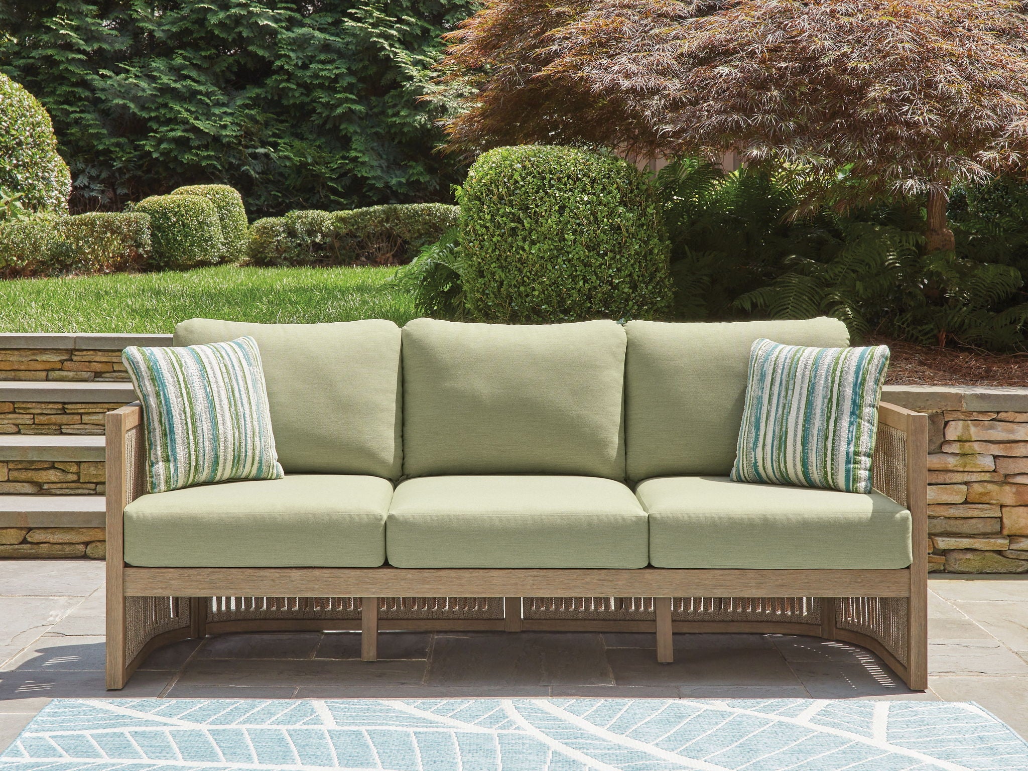 Outdoor sofa with light-green seat cushions, two striped pillows, and beige frame