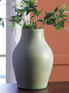 Green ceramic vase holding green stems and leaves