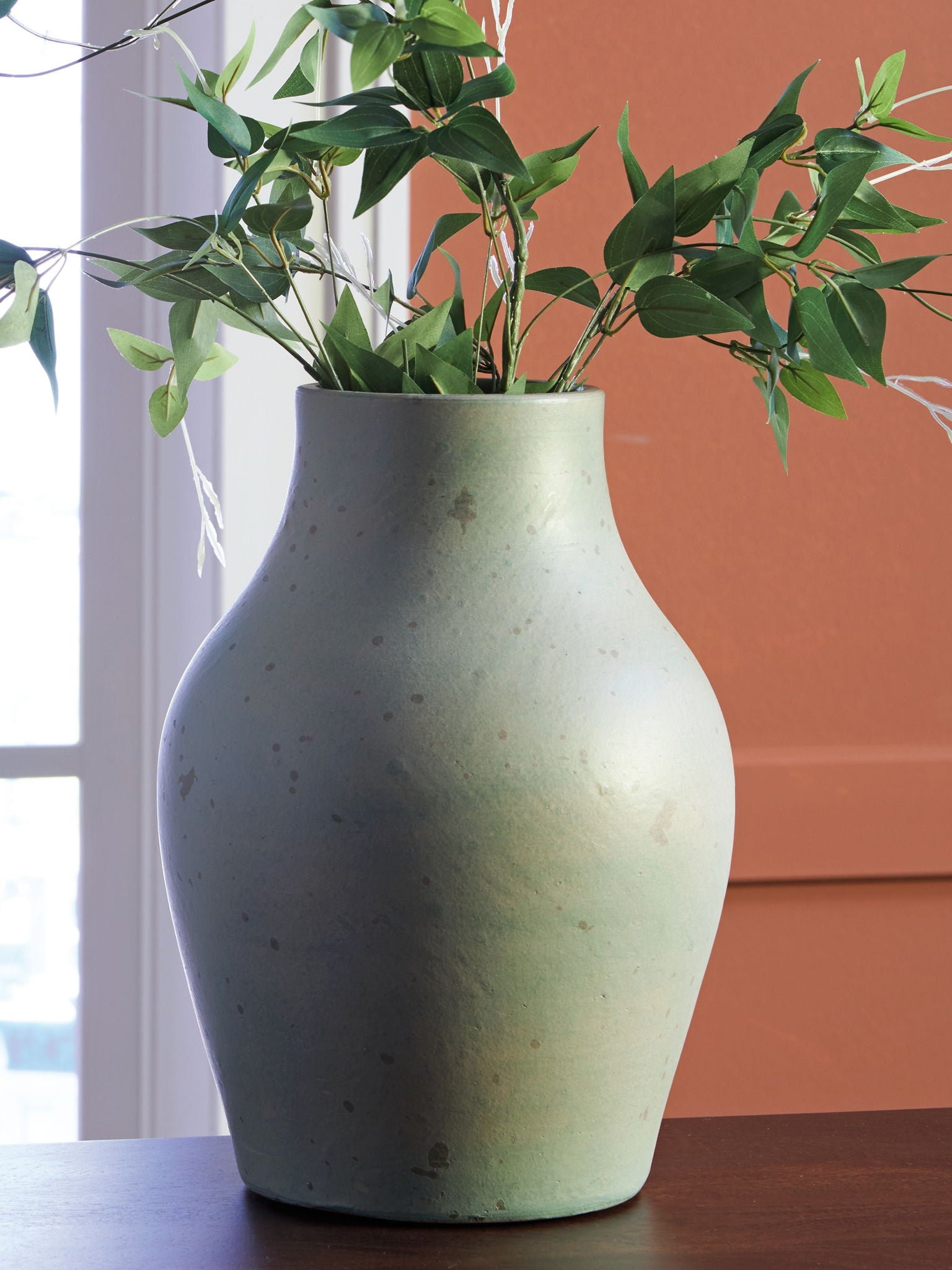 Green ceramic vase holding green stems and leaves