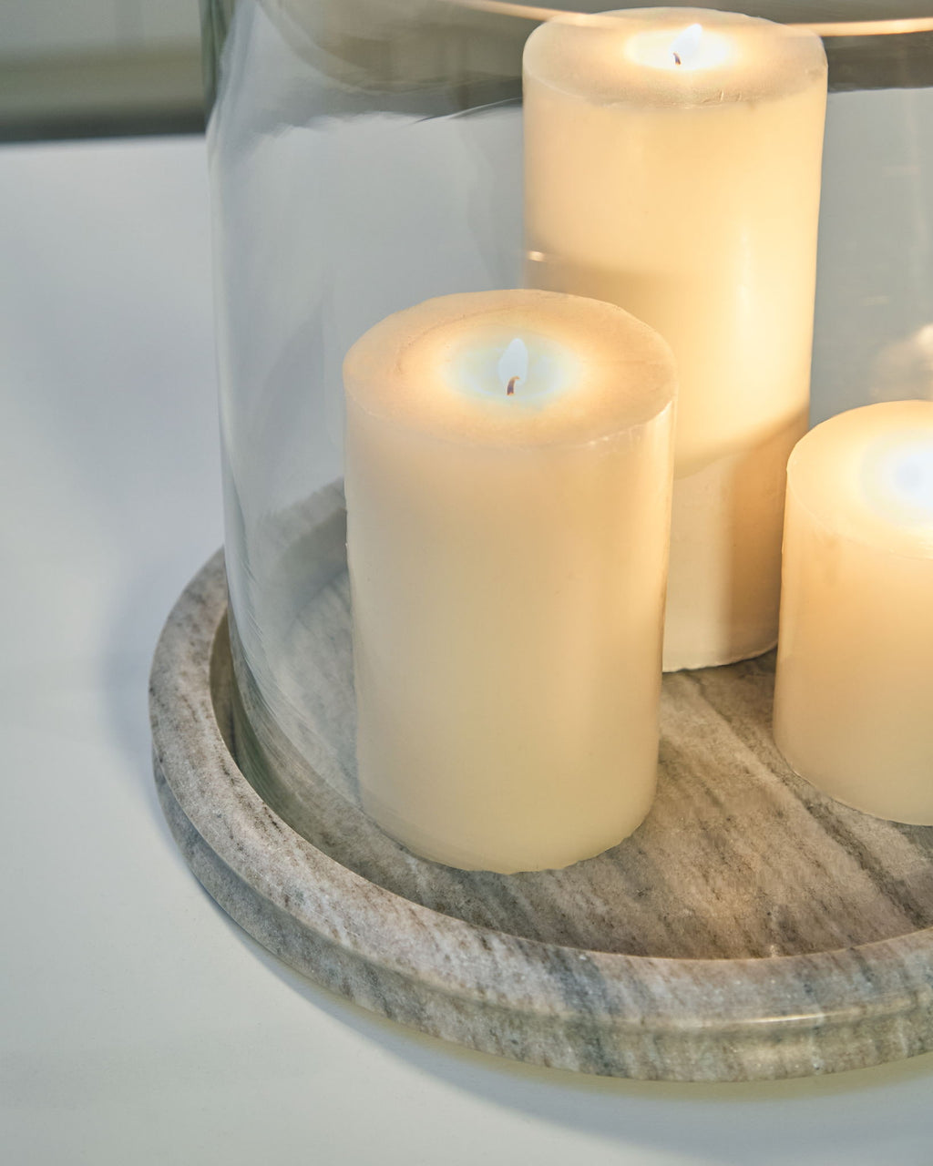 Glass cylinder candle holder with light stone base, holding lit white candles