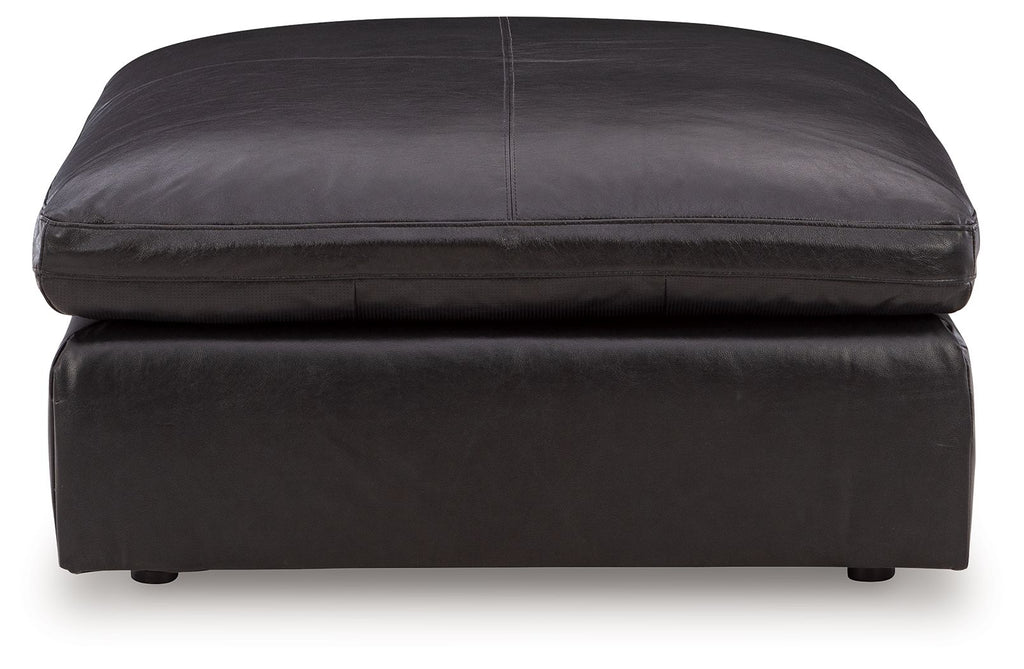 Black oversized accent ottoman with stitched top edge, rounded cushion, and visible legs