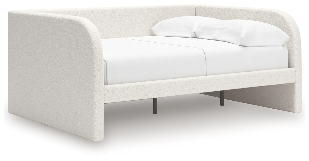 Upholstered day bed in beige fabric with white cushions; open underside with legs