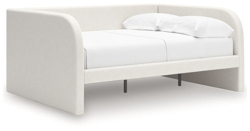 Upholstered day bed in beige fabric with white cushions; open underside with legs