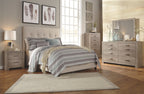 Gray upholstered queen bed with tufted headboard, patterned quilt, and pillows