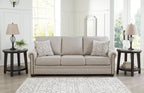 Light gray sofa with rolled arms and three decorative pillows, including patterned accents