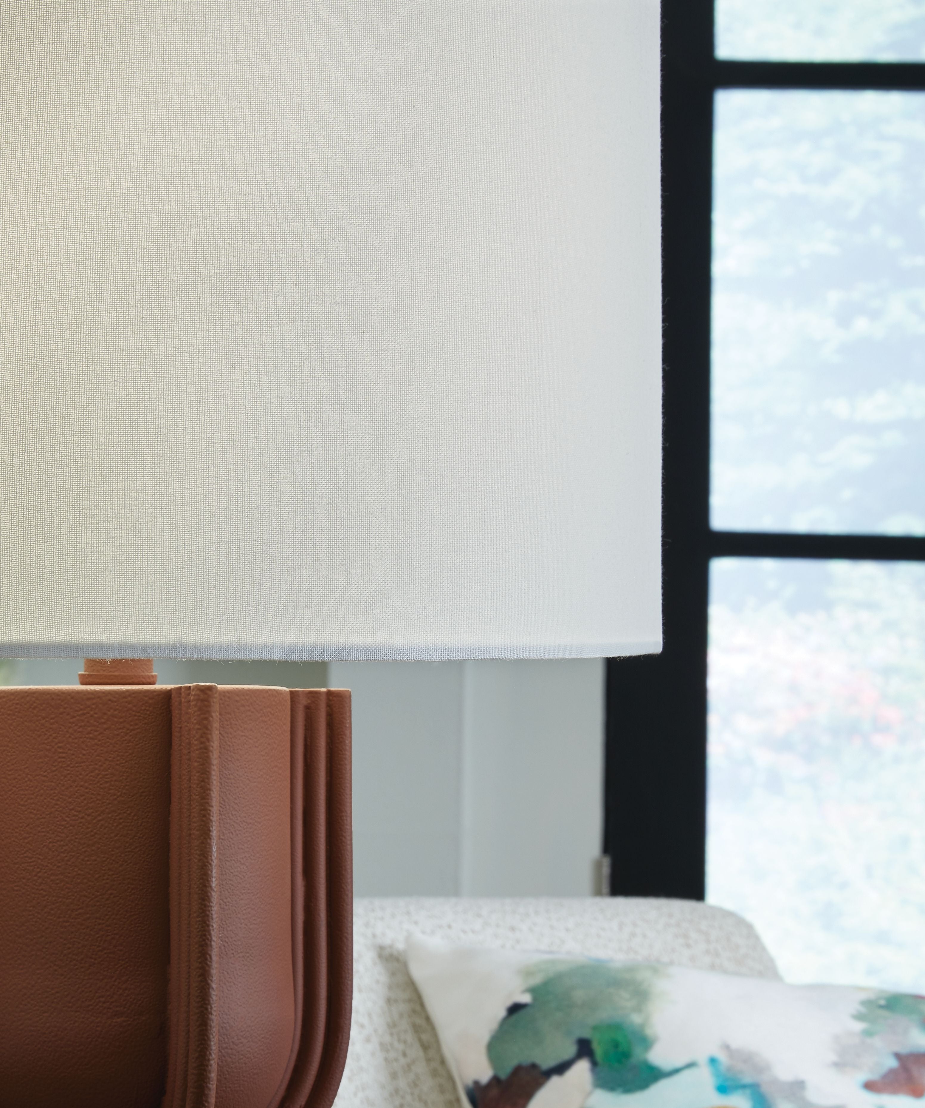 Brick-red metal table lamp base with white drum shade, close-up