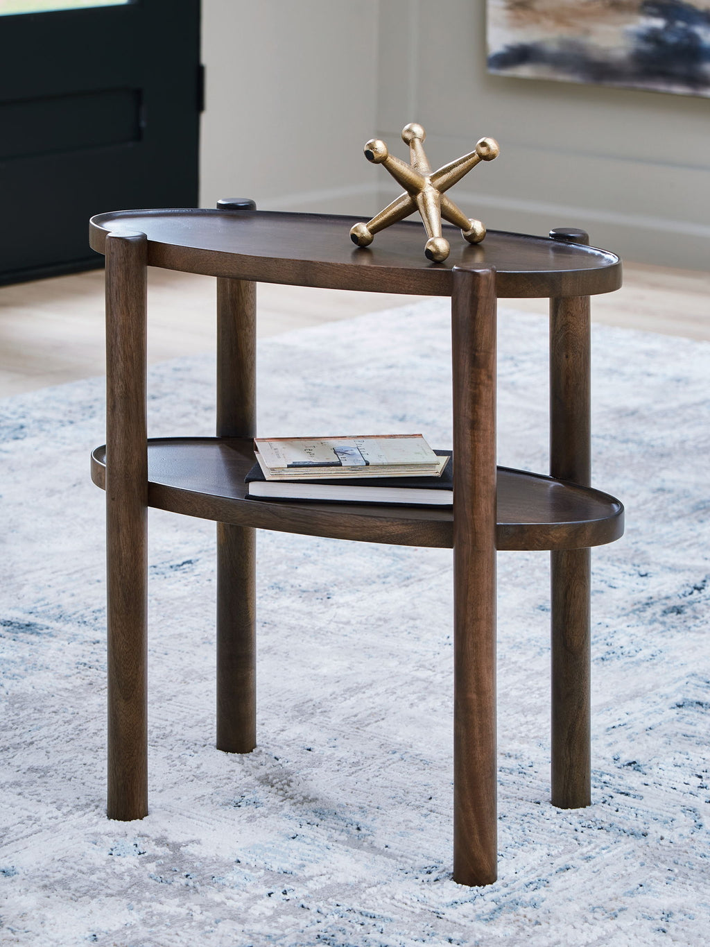 Gray-brown two-tier accent table with round top and lower shelf, styled with metal centerpiece