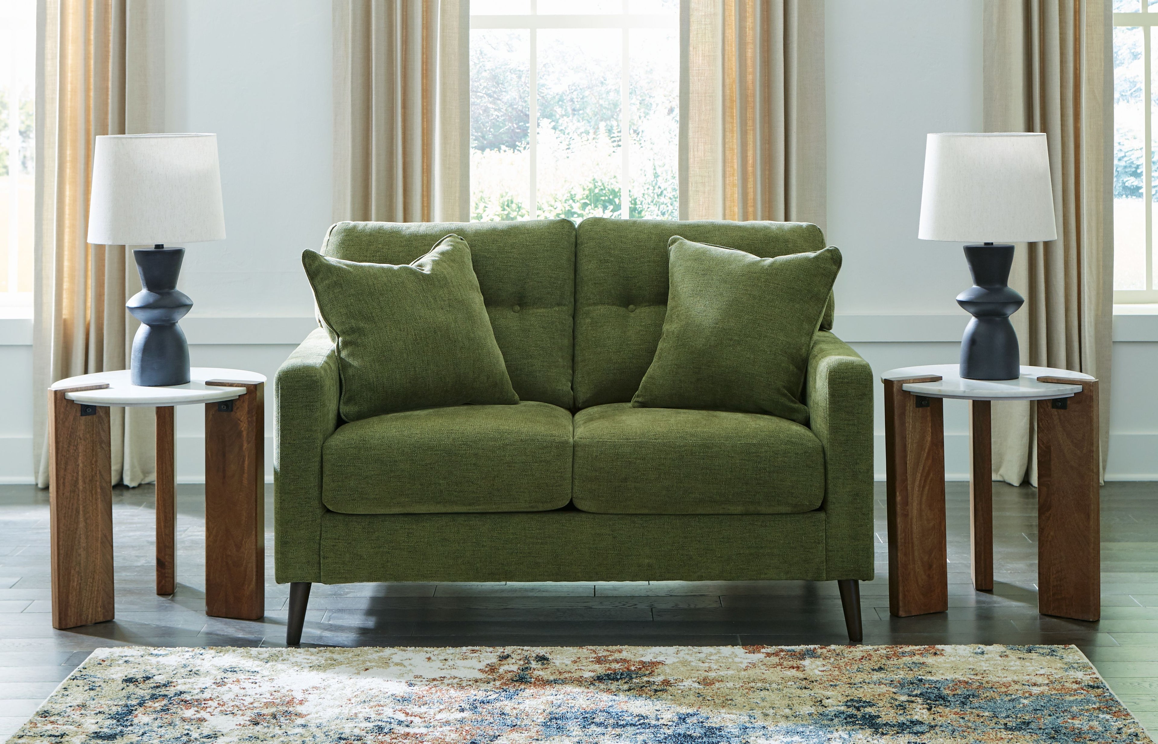 Green loveseat with tufted back and two seat cushions, styled with three throw pillows.