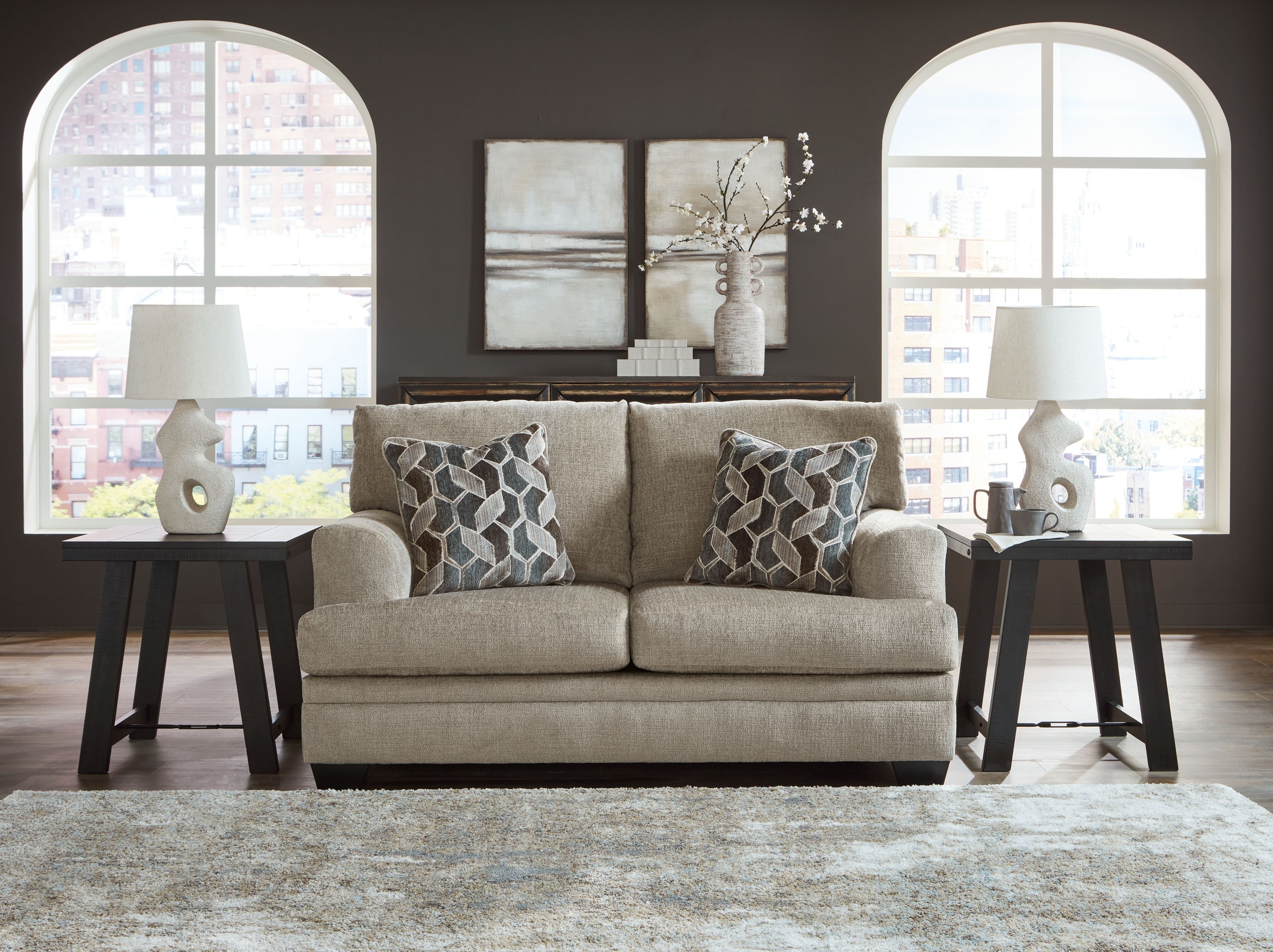 Light beige fabric loveseat with two geometric patterned pillows, centered view