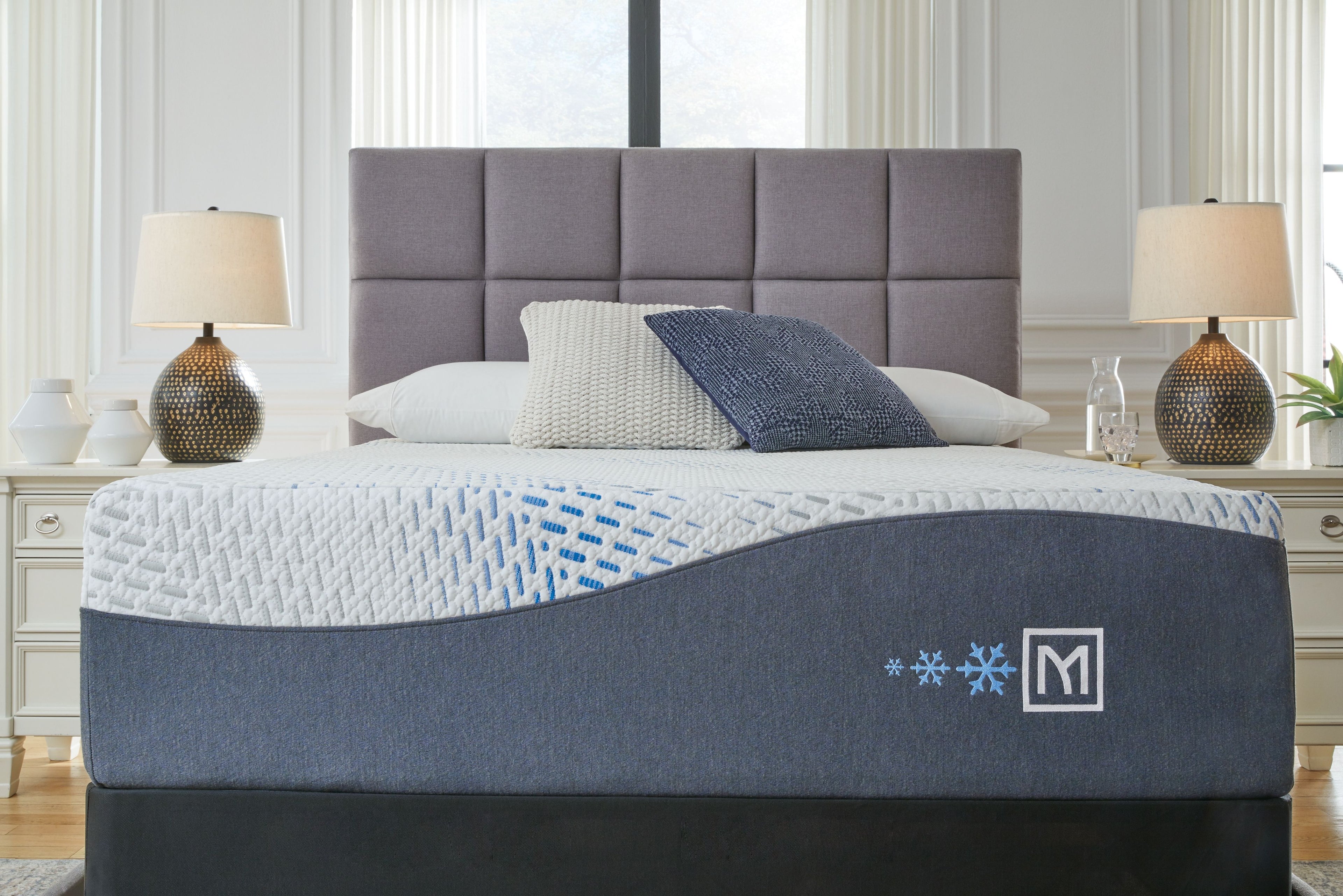 White plush mattress with dark gray side panels and logo, shown on a bed.