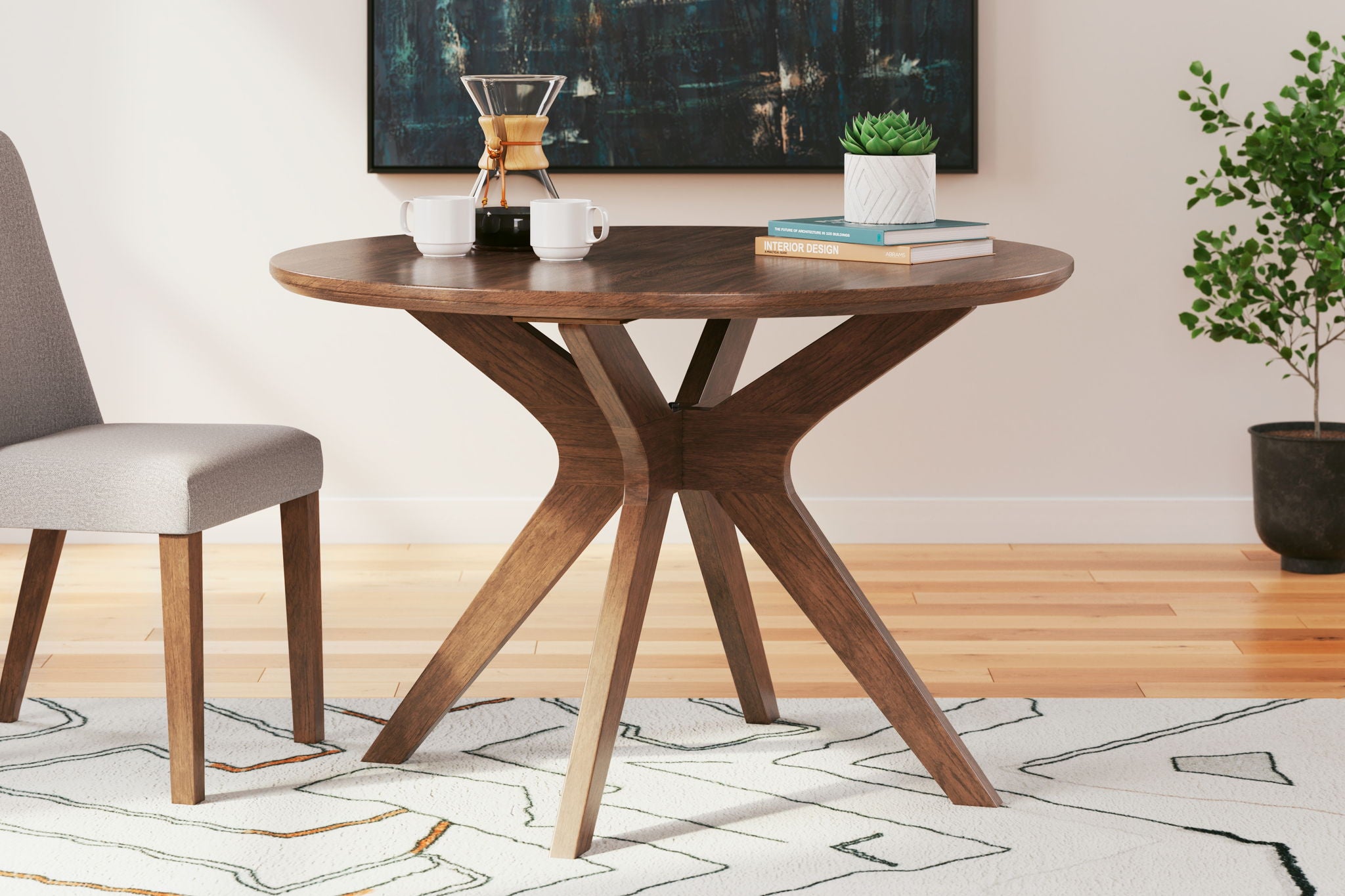 Round wood dining table with X-shaped pedestal and dark upholstered chair