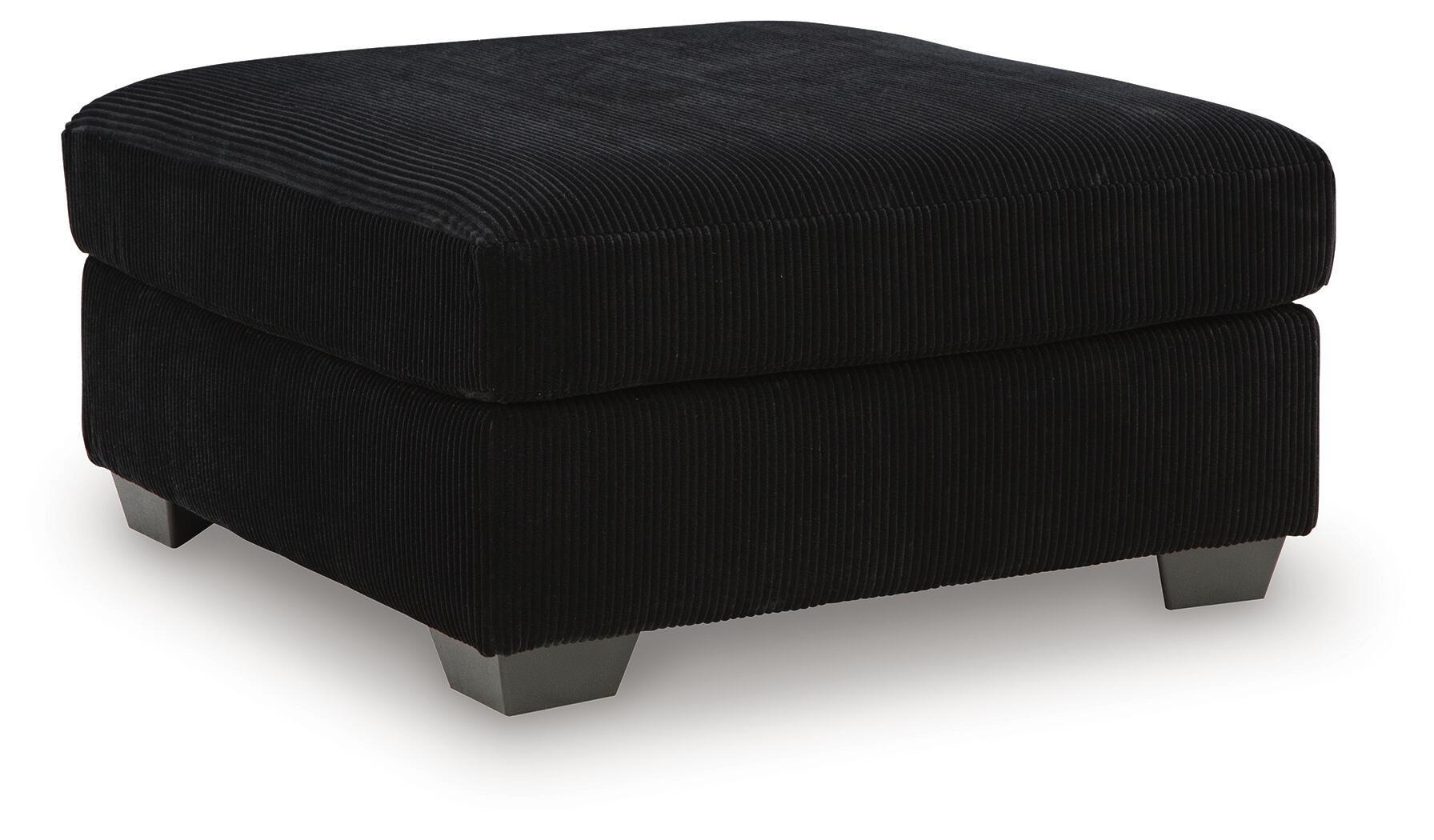 Black oversized ottoman with ribbed fabric, square padded top, dark legs.