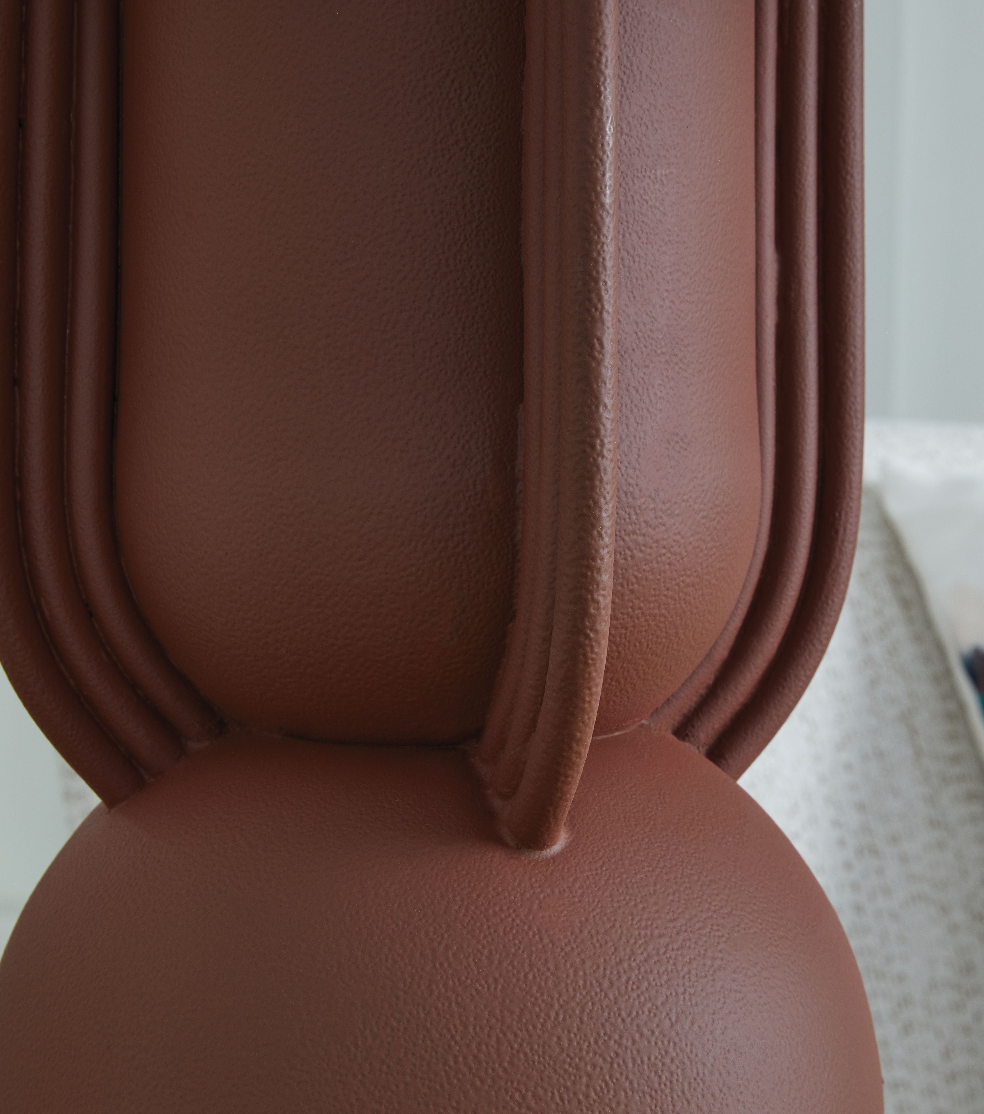 Brick-red metal lamp base with fluted columns, close-up detail