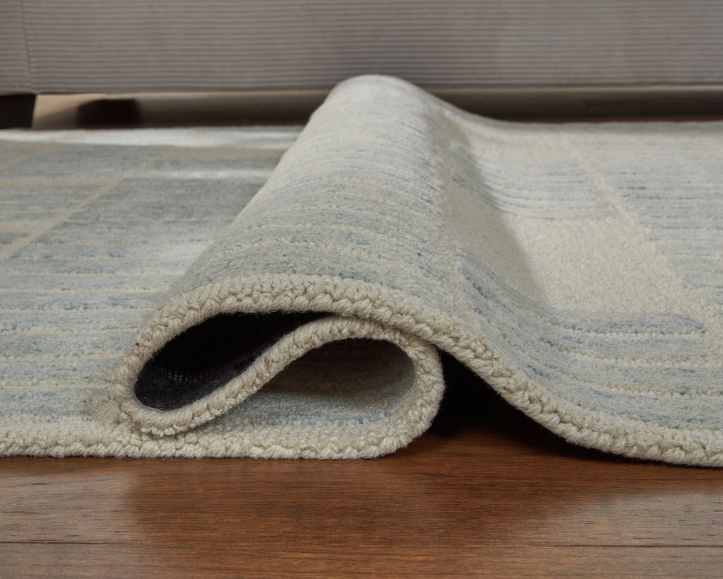 Light blue area rug with folded corner and repeating grid pattern, plush backing