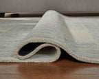 Light blue area rug with folded corner and repeating grid pattern, plush backing