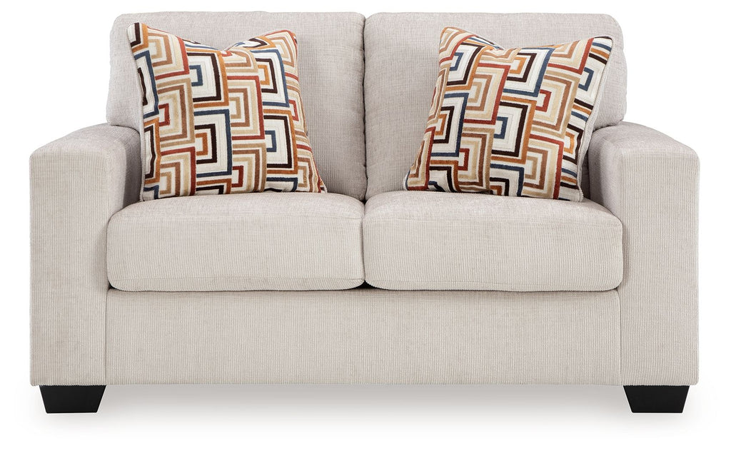 Light beige loveseat with two patterned throw pillows and low, squared arms.