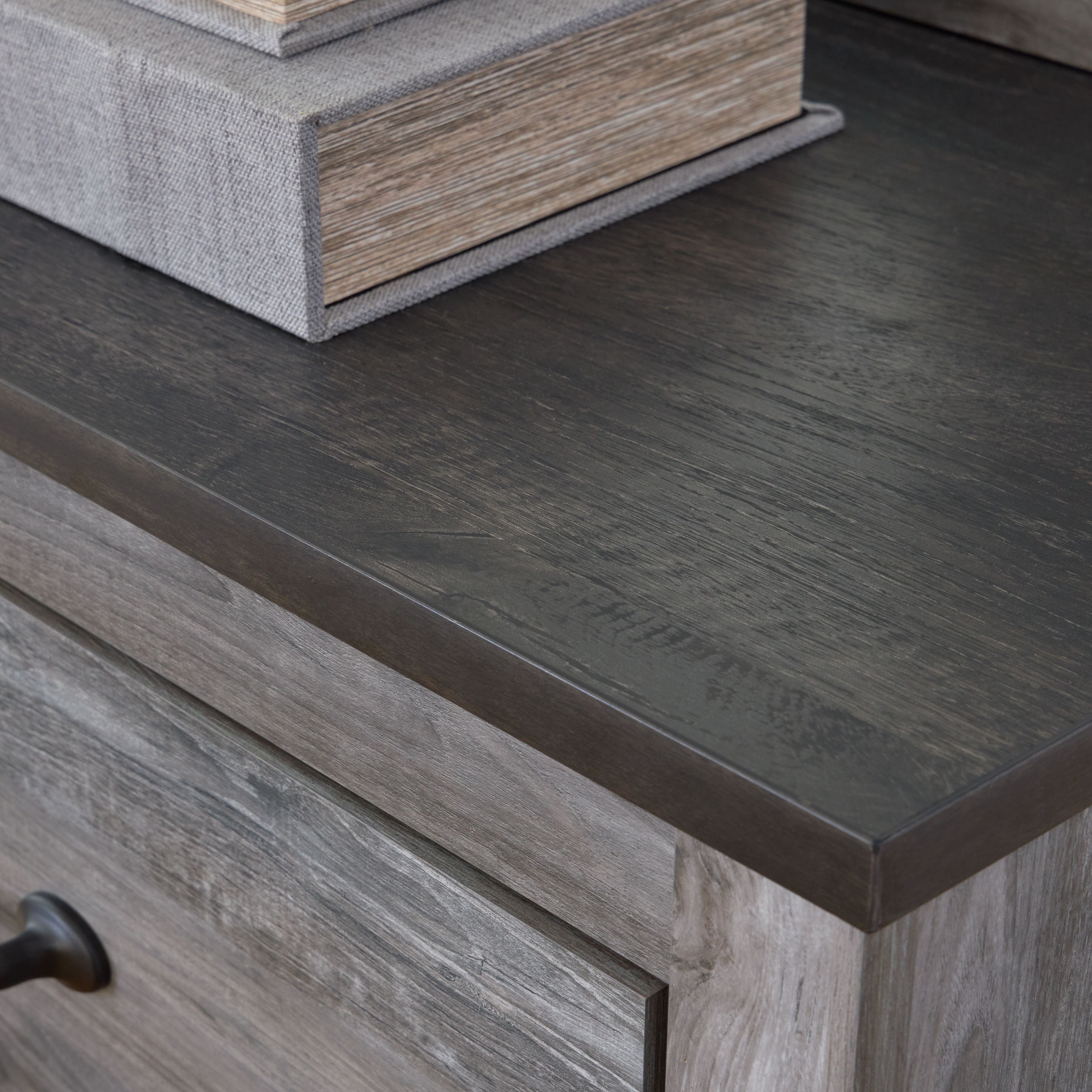 Dark gray wood dresser edge with drawer frame and metal bar pull, close-up