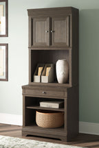 Weathered gray bookcase with double doors, open shelves, and drawer; styled with books and basket