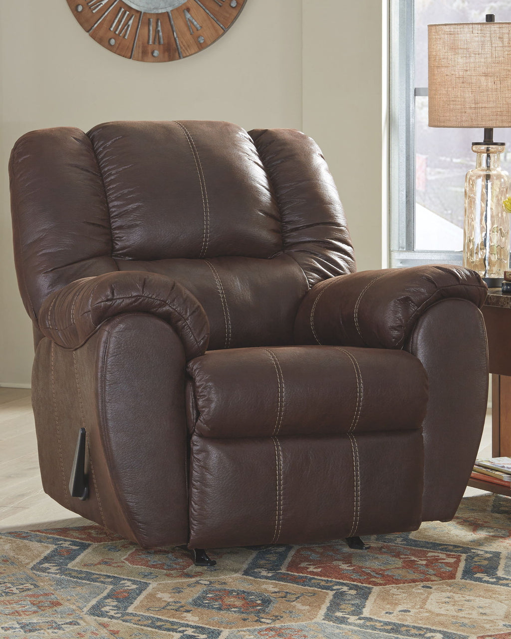 Brown leather rocker recliner with curved arms, tufted back, and extended footrest
