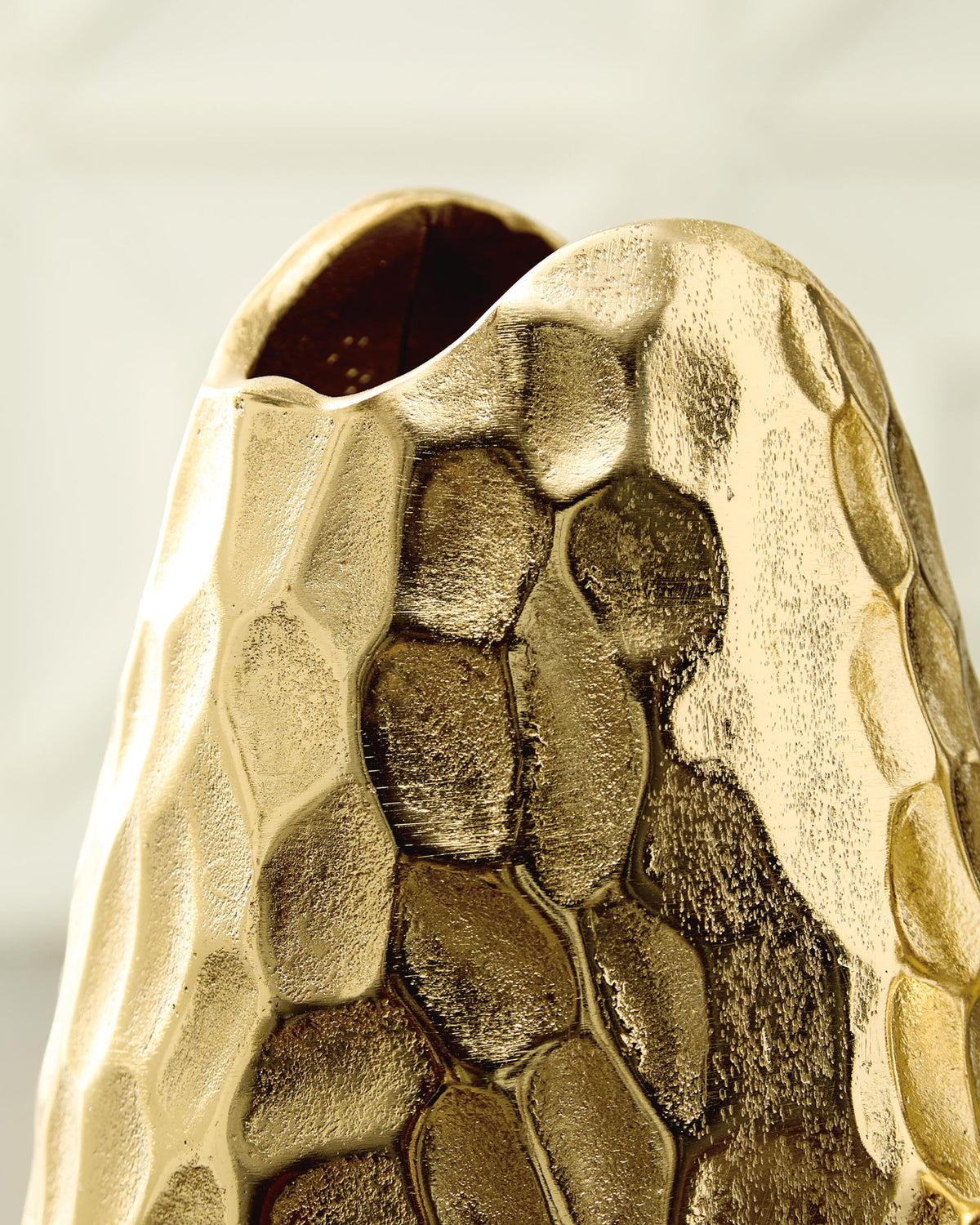 Gold hammered metal vase opening with dark interior and faceted texture