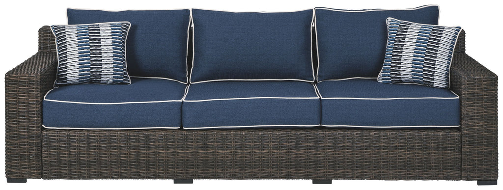 Three-seat brown wicker sofa with blue back cushions and two striped throw pillows