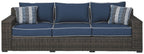 Three-seat brown wicker sofa with blue back cushions and two striped throw pillows