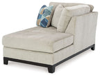 Stone corner chaise with wide seat, tufted back, dark legs, and geometric accent pillow