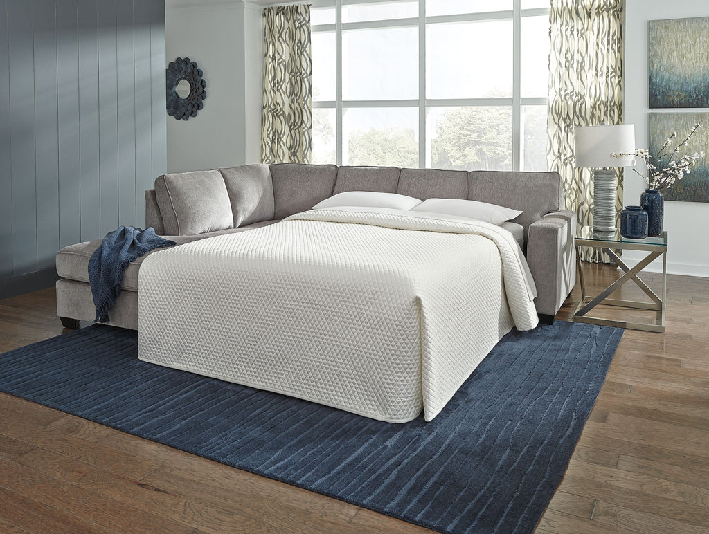 Grey sofa sleeper with white mattress pulled out and two throw pillows