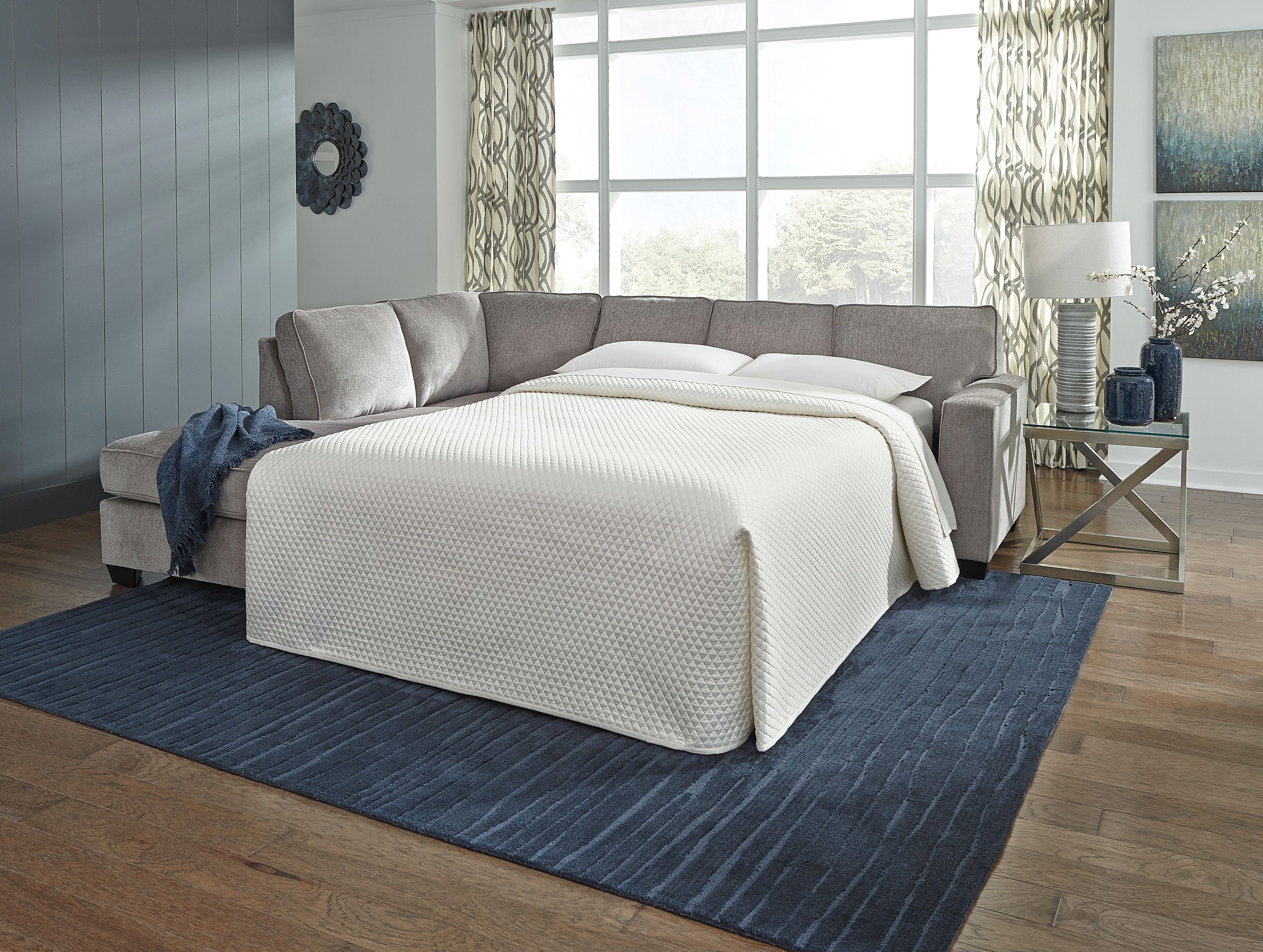 Grey sofa sleeper with white mattress pulled out and two throw pillows