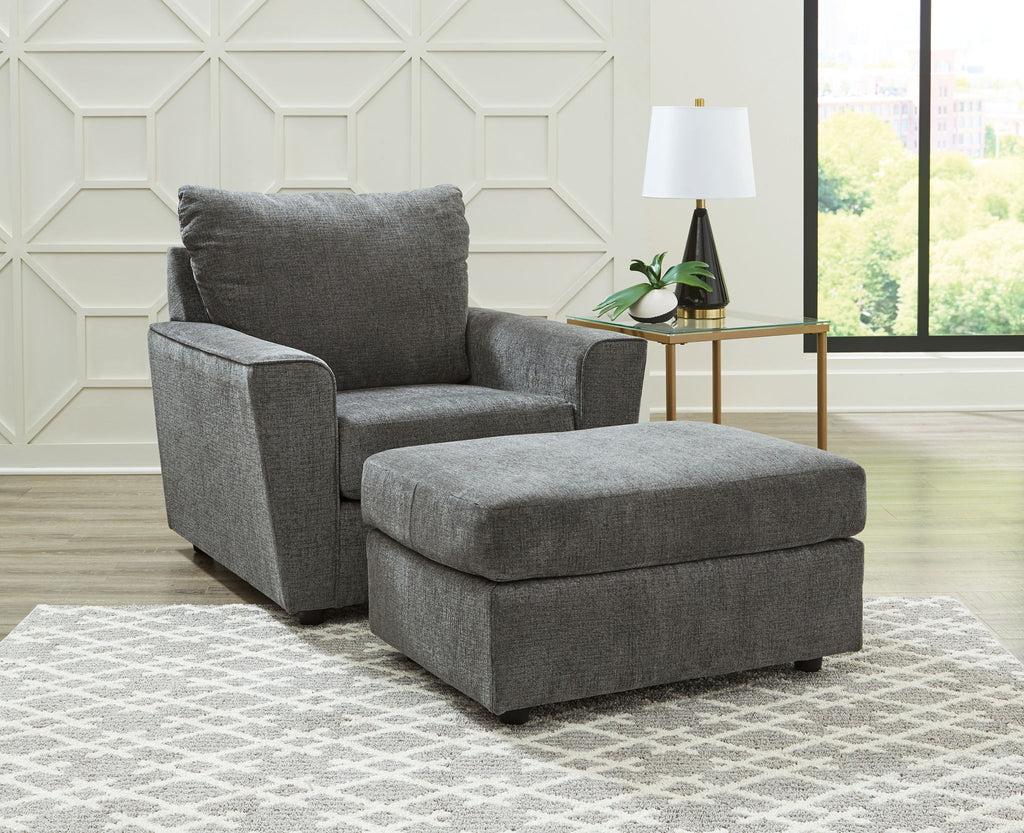 Dark gray fabric loveseat with ottoman and layered throw pillows.