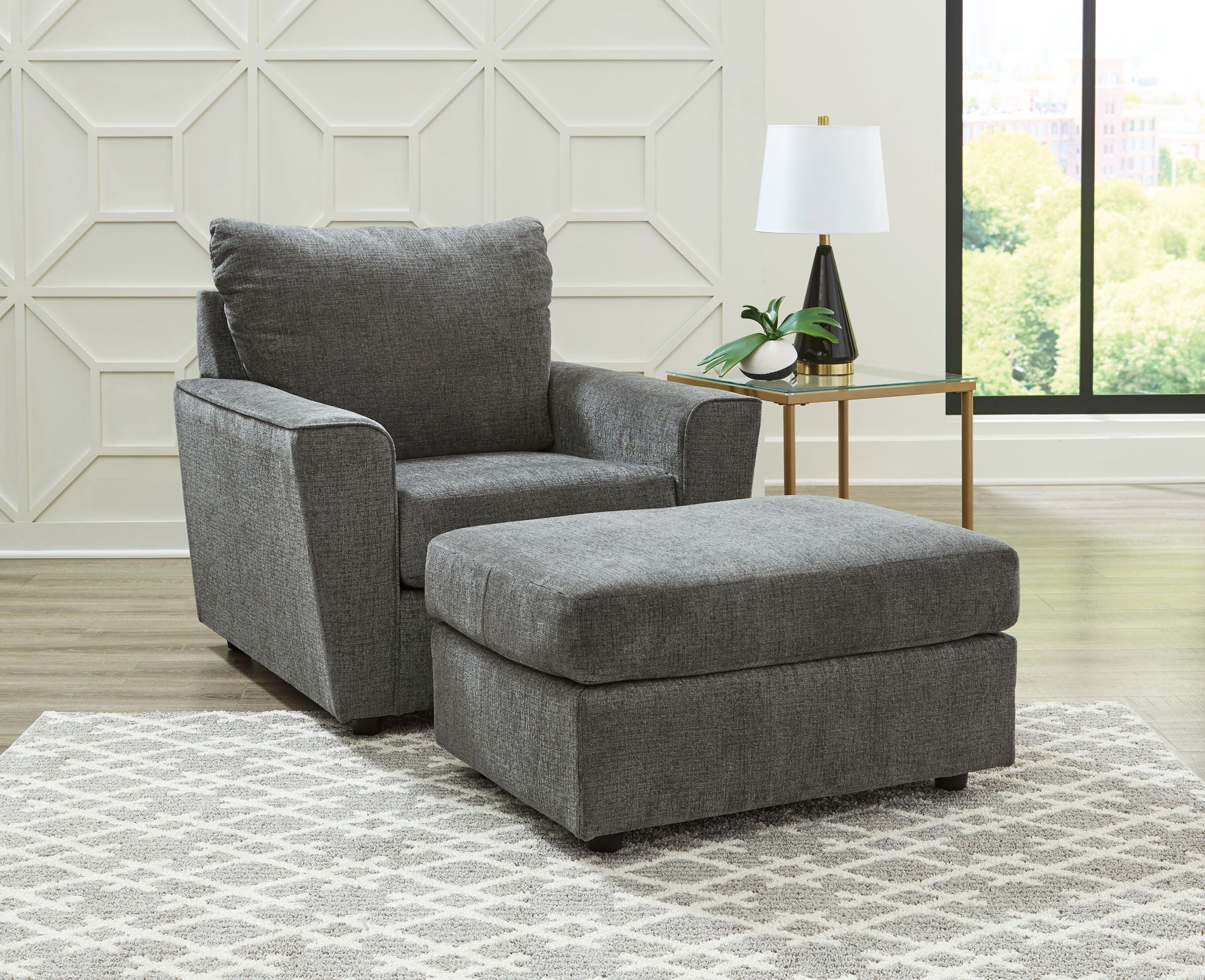 Dark gray fabric loveseat with ottoman and layered throw pillows.
