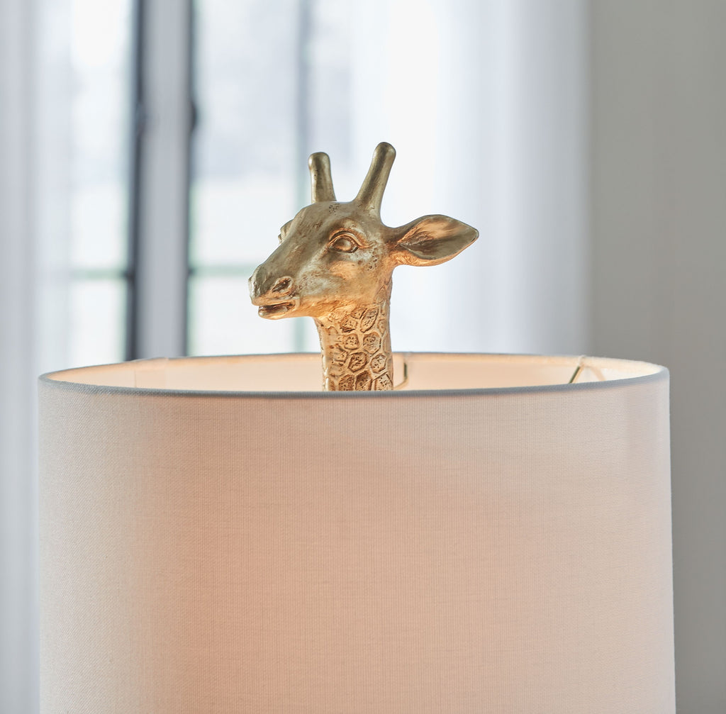 Gold table lamp with giraffe head detail and white fabric drum shade.
