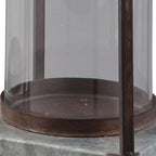 Clear glass cylinder lantern with dark metal frame and round brown base tray