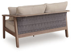 Natural beige loveseat with cushion, striped back pillows, wicker wrap base, armrests