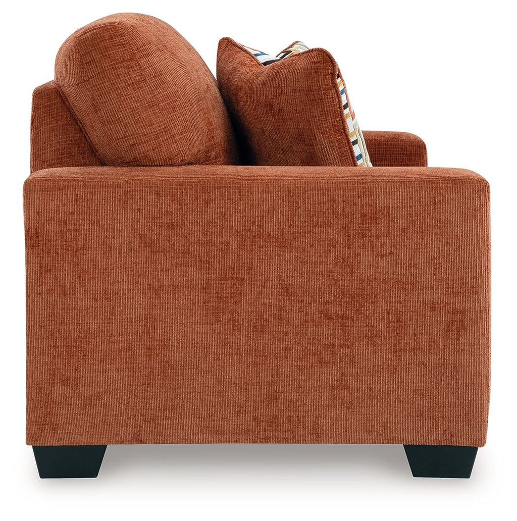 Rust orange loveseat with two decorative patterned throw pillows and rounded arms.
