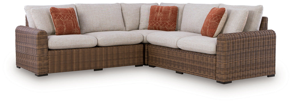Outdoor sectional sofa with beige cushions, brown wicker frame, and rust accent pillows