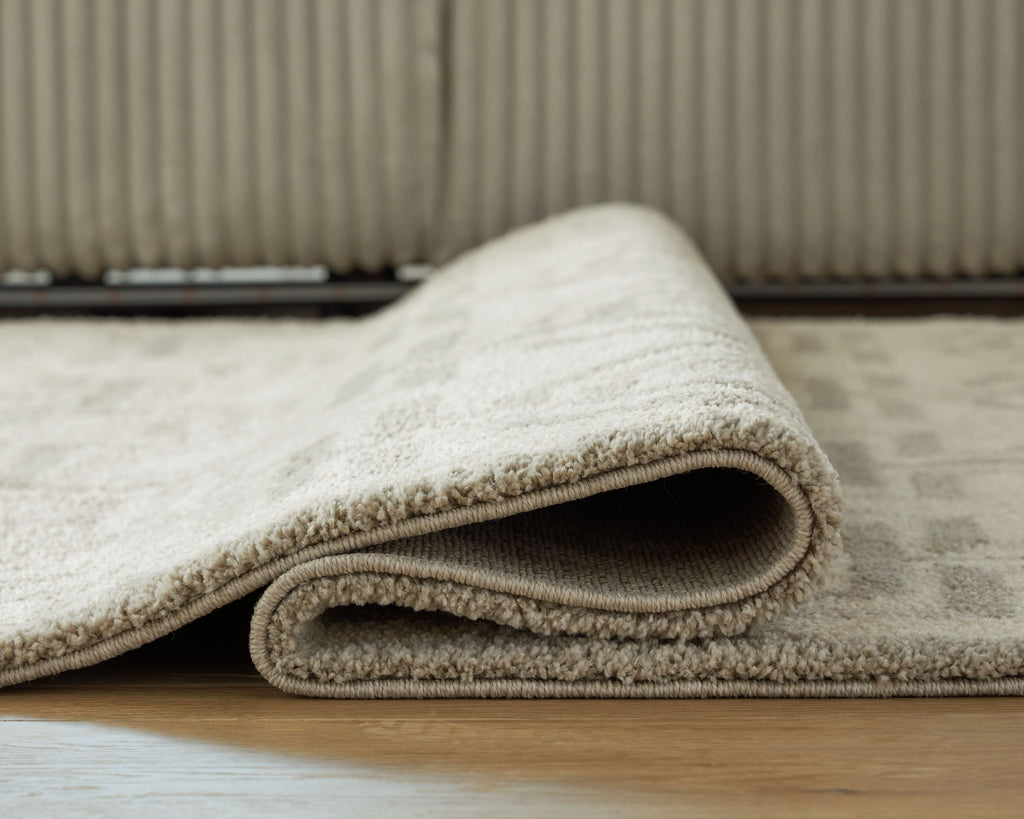 Beige rug with stitched border and low-pile texture, rolled edge detail