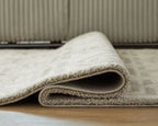 Beige rug with stitched border and low-pile texture, rolled edge detail