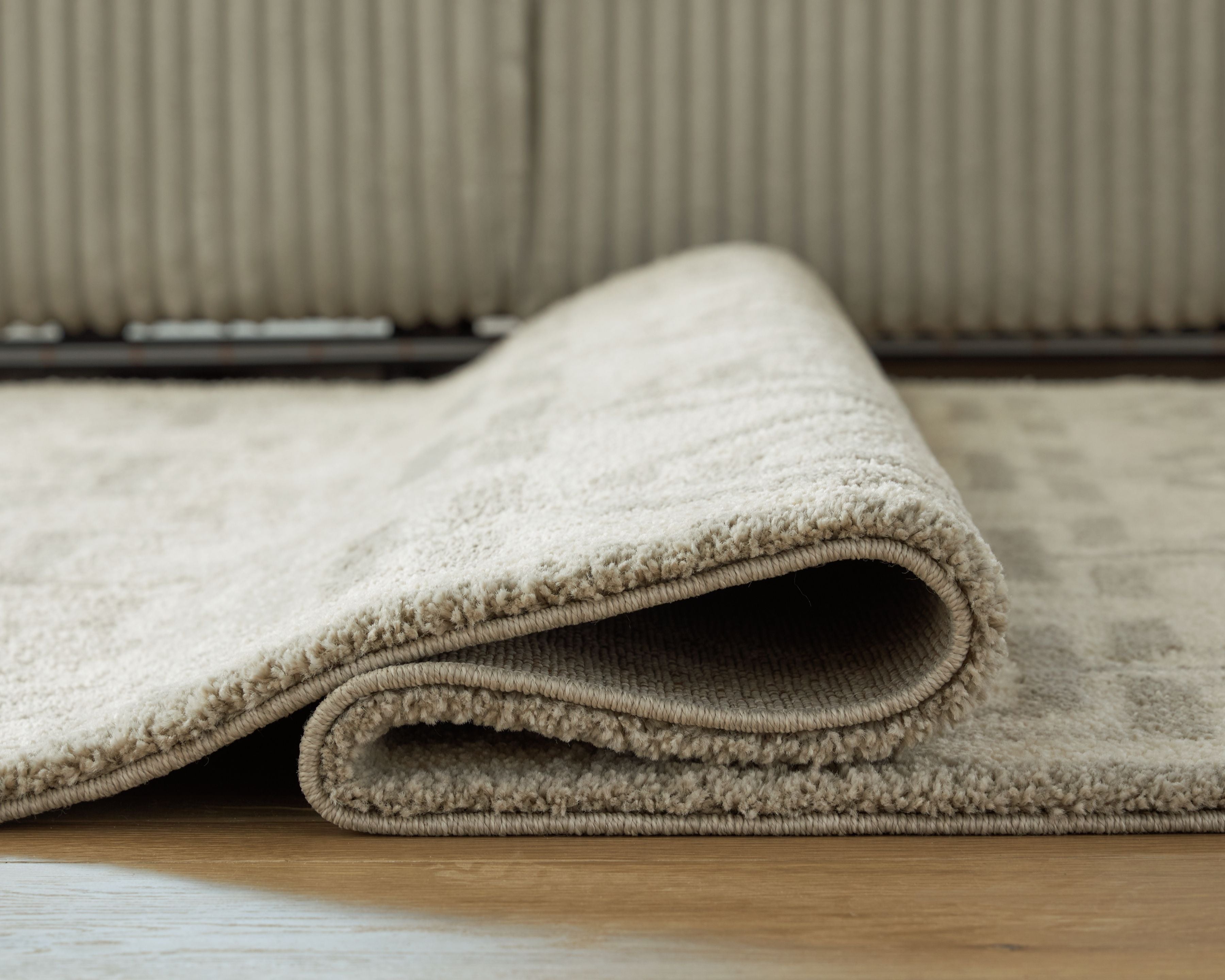 Beige rug with stitched border and low-pile texture, rolled edge detail