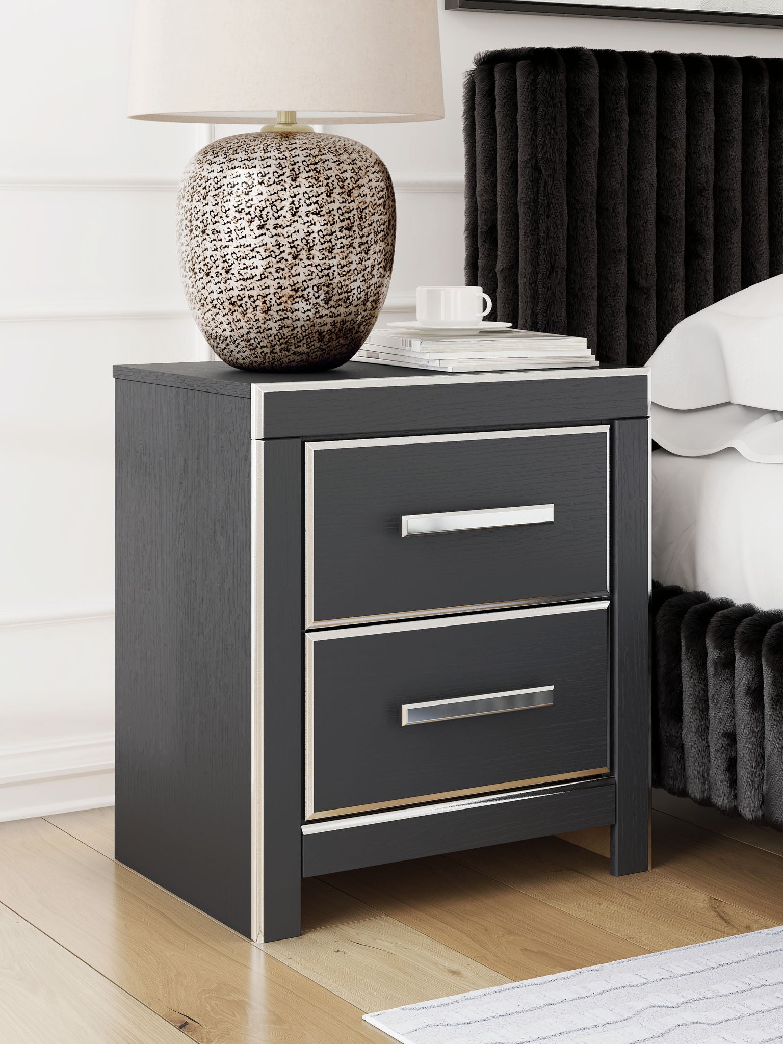 Black two-drawer night stand with two silver bar pulls beside a bed