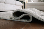 Gray area rug edge rolled up, showing low pile and rug backing