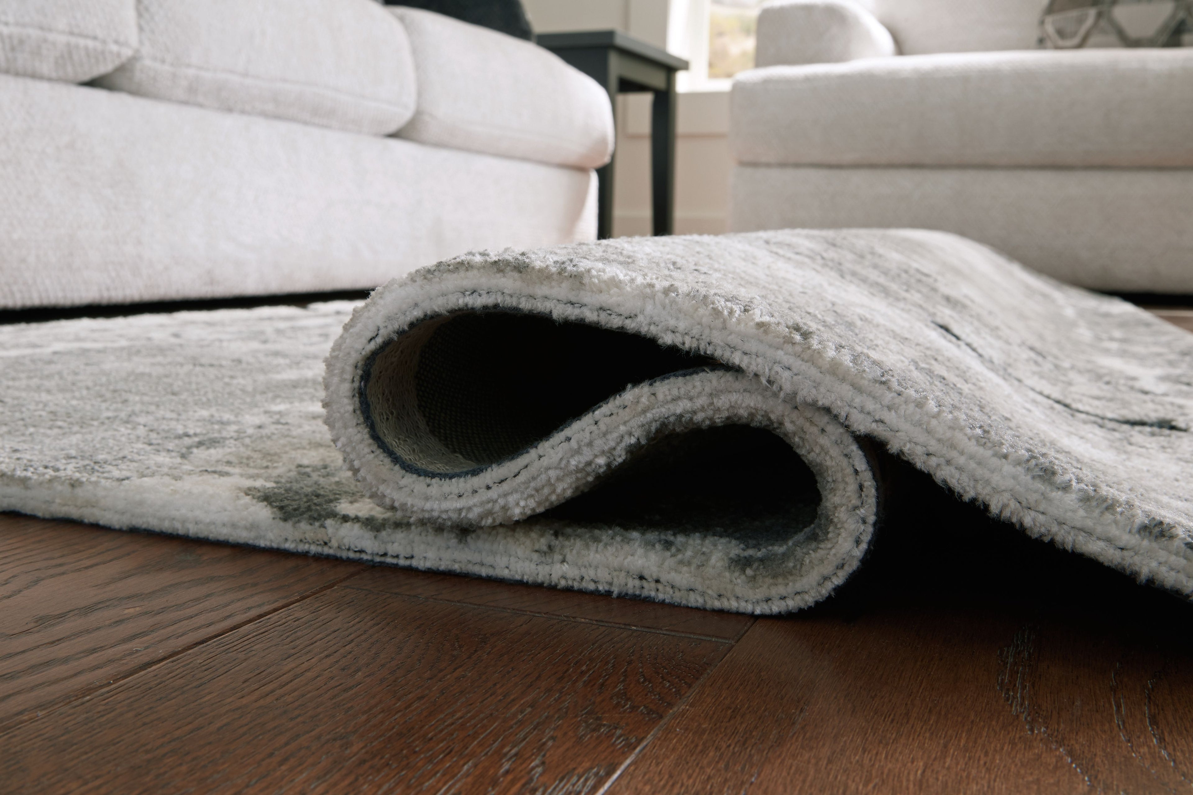 Gray area rug edge rolled up, showing low pile and rug backing