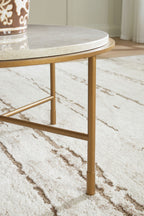 Round table corner view with cream stone-look top and gold metal cross-brace legs.