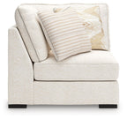 Corner chair with vanilla-beige fabric, single patterned pillow, and low dark feet