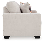 Light beige loveseat with two stacked back cushions and patterned throw pillow.